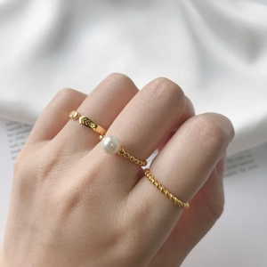 Detailed view of three gold rings featuring pearls and beaded V-patterns on a model's hand