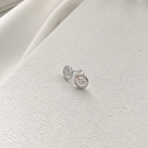 Close-up of S925 sterling silver smile face stud earrings on a textured background