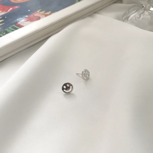 Detail view of silver S925 smiley face stud earrings on a soft white fabric background