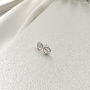 Close-up of minimalist S925 sterling silver smiley face stud earrings on white fabric