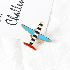 Détail du pin's avion en émail avec ailes bleues et bordure dorée sur fond textile
