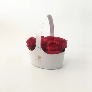 Close-up of a white envelope-style flower basket with red roses and gold accents