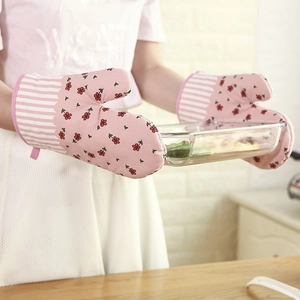 Floral oven mitts with pink flower patterns used to hold a glass tray in a kitchen