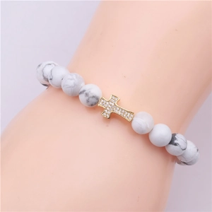 Detail shot of white turquoise beaded bracelet with gold cross pendant and zircon inlay
