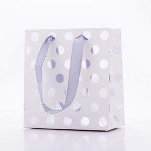 Sac cadeau en papier blanc avec pois argentés et anses en ruban satiné sur fond blanc