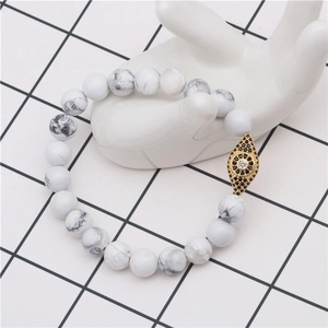 Detail shot of a white turquoise beaded bracelet featuring a gold evil eye charm with cubic zirconia