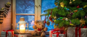 Cosy Christmas scene featuring a warm lantern, teddy bear, and red ribbon gift boxes