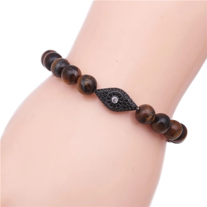Close-up of tiger eye stone bead bracelet with a black zircon evil eye charm on wrist