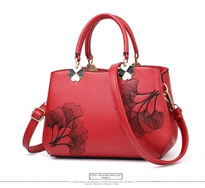 Detail of leaf pattern embroidery on wine red leather shoulder bag with clover ornament