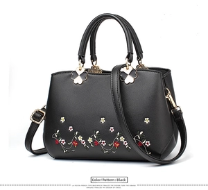 Detail of black handbag with colorful floral embroidery and clover charms on zippers