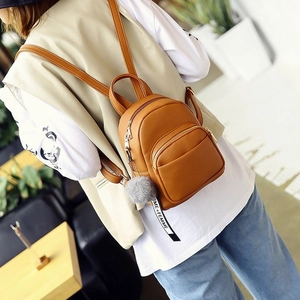 Detail of a brown leather mini backpack with a grey fur ball charm and woven strap
