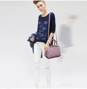 Close-up of purple handbag with floral embroidery and gold hardware held by a model