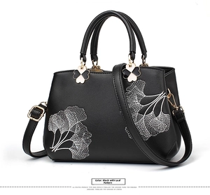 Detailed embroidery of white ginkgo leaves on a black textured leather crossbody handbag