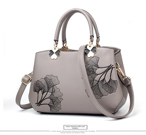 Close-up of the grey faux leather handbag showing embroidery and clover hardware