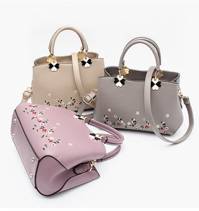 Detail of PU leather handbags with floral embroidery and clover-shaped metal hardware