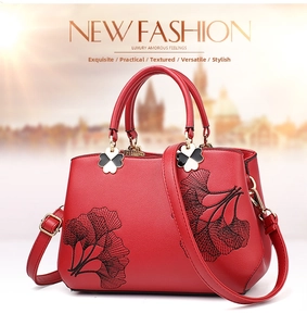 Macro shot of red pebble leather handbag with black ginkgo leaf embroidery and clover charm