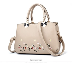 Detail of khaki leather handbag featuring floral embroidery and lucky clover charm