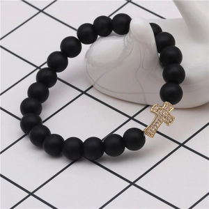 Detail shot of matte black beaded bracelet featuring a gold plated zircon cross charm