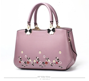 Detailed 45-degree side view of purple handbag with floral embroidery and clover charms