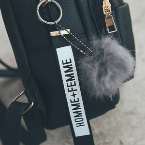 Detail of black leather backpack with gold zipper, grey pompom and white woven label tag