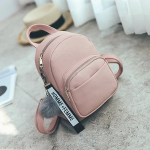 Pink mini PU leather backpack with grey pompom charm and top handle on textured background