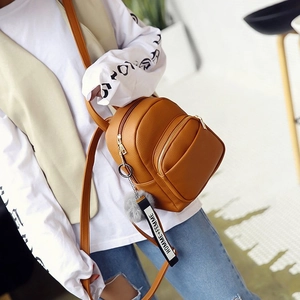 Brown PU leather mini backpack with a grey fur pompom and logo ribbon worn cross-body