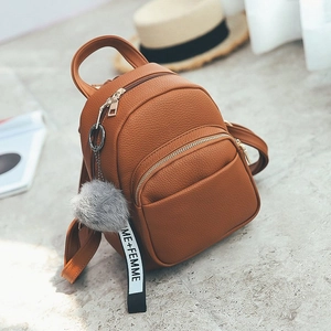 Detail view of brown lychee-patterned PU leather backpack with a grey fur pom pom keychain