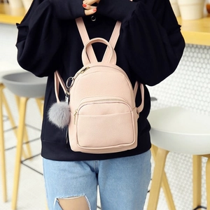 Pink mini PU leather backpack with gold zippers and grey fur ball accessory on a model