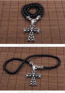 Detailed view of silver skull cross pendant necklace on black beaded chain with bamboo background