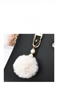 Detailed close-up of a white fluffy pompom charm with pearls on a black leather bag