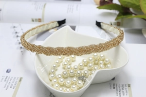 Detail of golden woven beaded headband placed on a white leaf tray with elegant pearls