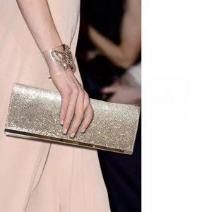 Detail showing hand holding champagne gold sequin evening clutch with metallic bottom trim