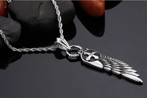 Detailed close-up of wings and cross pendant on a twist chain over pebbles