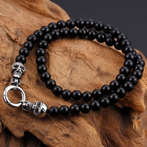 Polished black bead punk bracelet featuring vintage silver skulls and spring clasp on wood