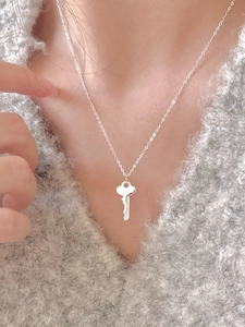 Close-up of minimalist S925 sterling silver key pendant necklace on a grey sweater