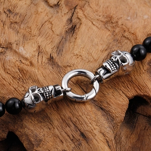 Punk style black bead bracelet featuring silver metal skull accents on rustic wood background