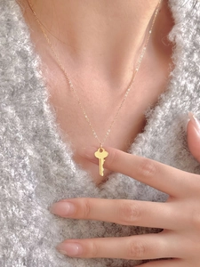 Detailed view of a golden key pendant necklace worn over a textured grey knit sweater