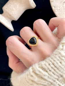 Détail d'une bague coeur en onyx noir avec bordure dorée sur un pull en maille douce