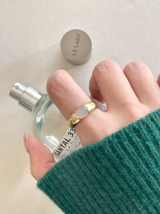 Close-up of golden wide band ring with oval white crystal worn with green sweater
