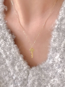 Detailed view of a gold key pendant necklace styled on a soft grey knitted sweater