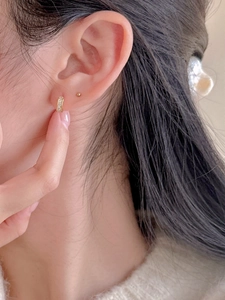 Close-up of minimalist gold zircon hoop earrings and bead studs worn on ear lobe