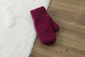 Dettaglio di muffole in lana lavorata a maglia bordeaux su legno e finta pelliccia