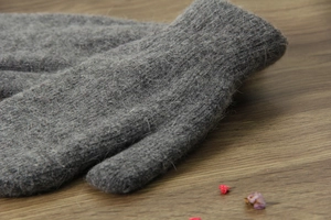 Dettaglio di muffole in maglia grigia con morbida trama felpata su fondo legno