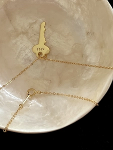 Detailed close-up of a S925 sterling silver key pendant with gold plating on a shell plate