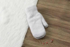 Dettaglio di un guanto in maglia bianca in pelliccia di coniglio su legno e peluche