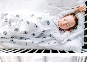 Détail de l'emmaillotage en mousseline blanche avec flocons verts sur bébé qui dort