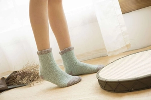 Détail de chaussettes en polaire corail vert menthe portées dans un salon douillet