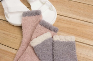 Détail de chaussettes douces en polaire corail rose et grise sur un sol en bois