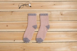 Gros plan de chaussettes épaisses en polaire corail rose et gris sur fond en bois
