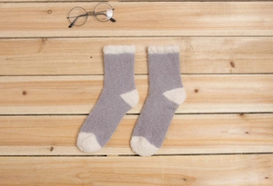 Détail de chaussettes en polaire corail grises et blanc cassé sur fond de bois